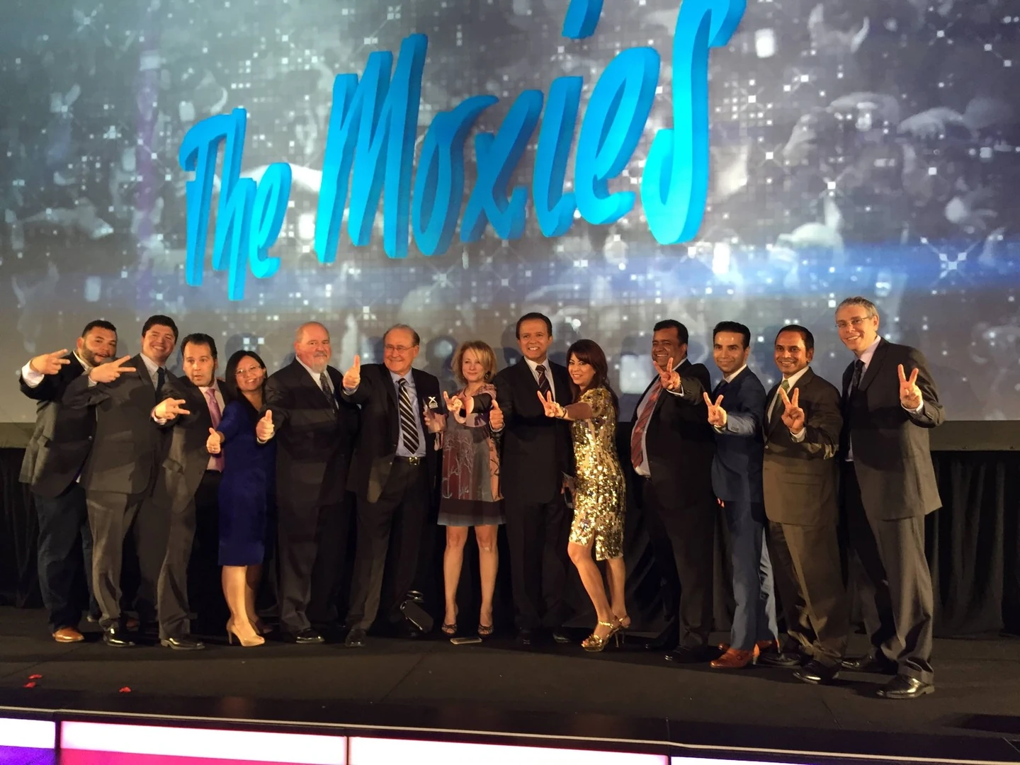 A group gathered onstage beneath The Moxies sign at an awards event